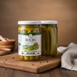 Dos frascos de vidrio con Pepinos Salvajes Encurtidos (Pickled Wild Cucumber) de la marca Koura Valley, mostrando los pepinos alargados en salmuera con la tapa blanca.