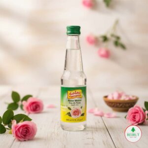 Botella de vidrio de Agua de Rosas Yamama 300ml con tapa verde, en fondo claro con pétalos de rosa. Producto de cocina árabe y cosmética natural.