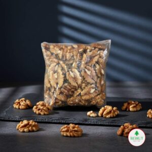 Bolsa transparente sellada de nueces peladas de nogal, con mitades de nueces esparcidas sobre una tabla oscura de pizarra.