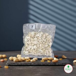 Bolsa transparente sellada al vacío llena de almendras peladas (blanqueadas), de color blanco cremoso, sobre una tabla oscura de pizarra.