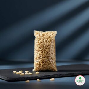 Bolsa de plástico transparente llena de piñones pelados y de color crema, con algunos piñones dispersos sobre una tabla negra de pizarra.