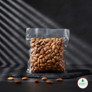 Bolsa transparente sellada al vacío llena de almendras enteras, con algunas almendras esparcidas sobre una tabla negra de pizarra.