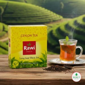 Caja de té negro Rawi Ceylon Tea de hoja larga sobre una mesa de madera rústica, junto a una taza de té humeante y hojas secas, con un fondo desenfocado de campos de cultivo de té verdes bajo un cielo despejado.