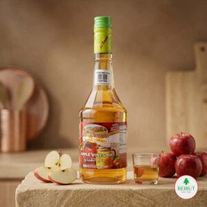 Botella de vidrio de Vinagre de Manzana Al Dayaa de 500ml con tapa verde, rodeada de manzanas rojas frescas.