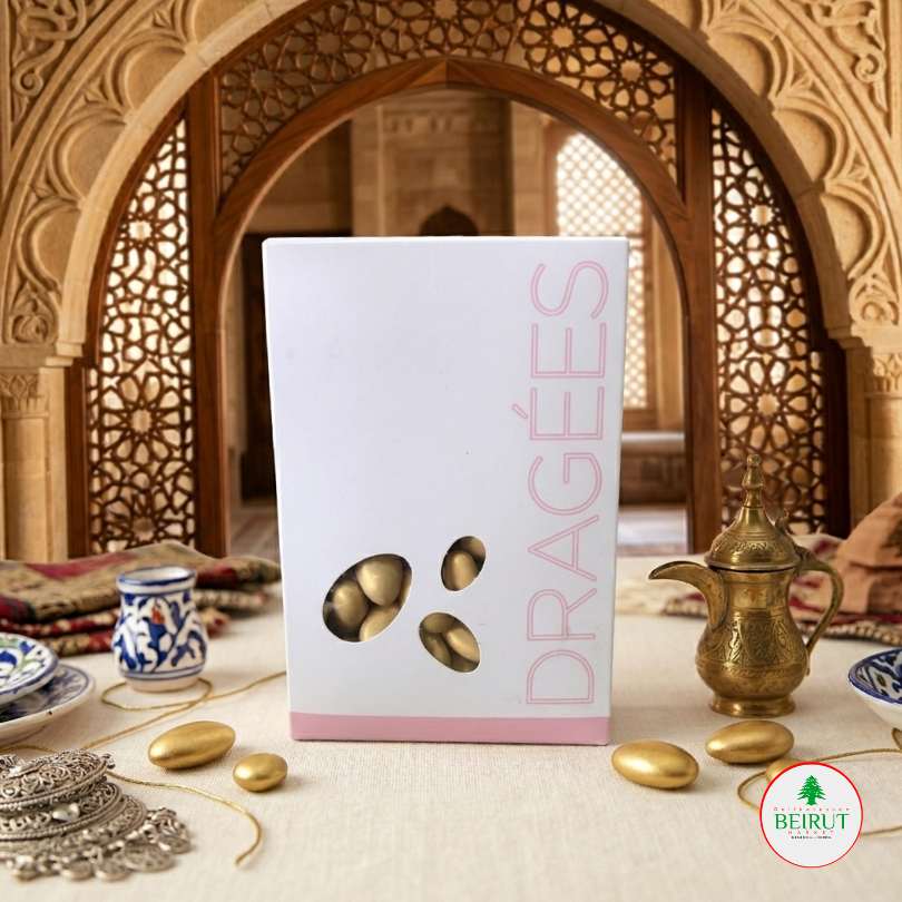 Caja blanca de Dragées con diseño minimalista y ventana que muestra almendras confitadas dorado, dispuesta en una mesa con decoración árabe tradicional y una cafetera de bronce al fondo.