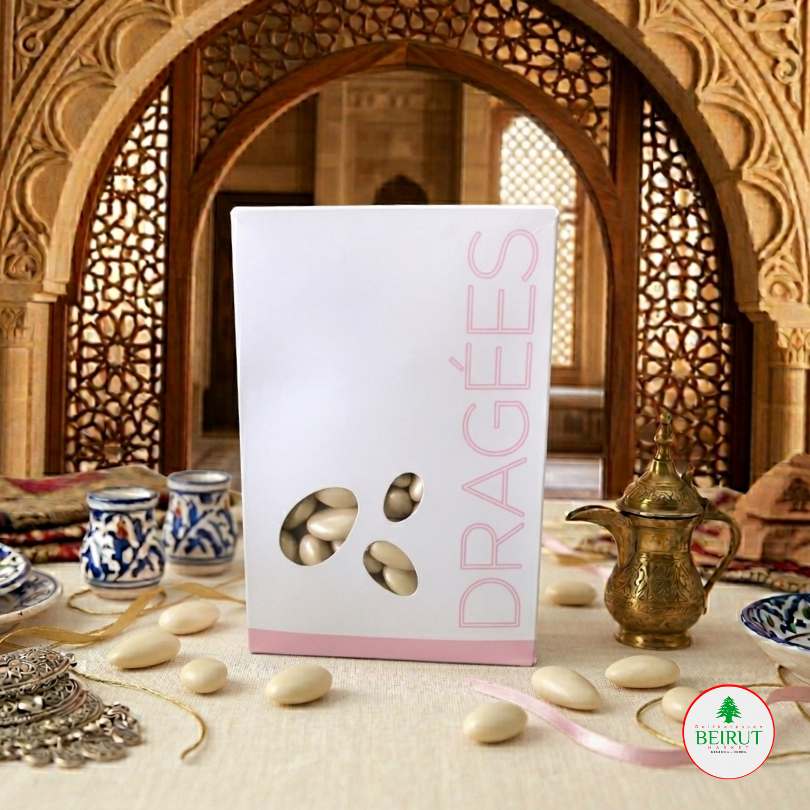 Caja blanca de Dragées con diseño minimalista y ventana que muestra almendras confitadas blanca, dispuesta en una mesa con decoración árabe tradicional y una cafetera de bronce al fondo.