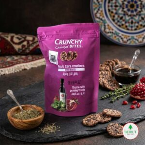 Bolsa de color violeta de snacks 'Crunchy Bites' de arroz y maíz con sabor a tomillo y granada, dispuestos sobre una tabla de piedra negra junto a granadas frescas