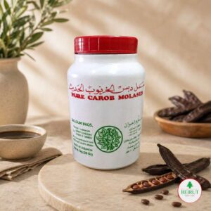 Frasco blanco de melaza de algarroba pura Salloum Bros de 1kg con vainas de algarroba y un cuenco pequeño sobre mesa de mármol.