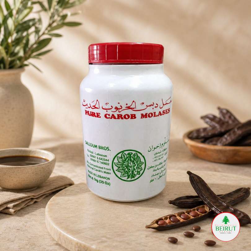 Frasco blanco de melaza de algarroba pura Salloum Bros de 1kg con vainas de algarroba y un cuenco pequeño sobre mesa de mármol.