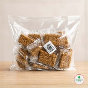 Bolsa transparente con 10 barritas individuales de dulce de ajonjolí tostado sobre una base de madera clara.